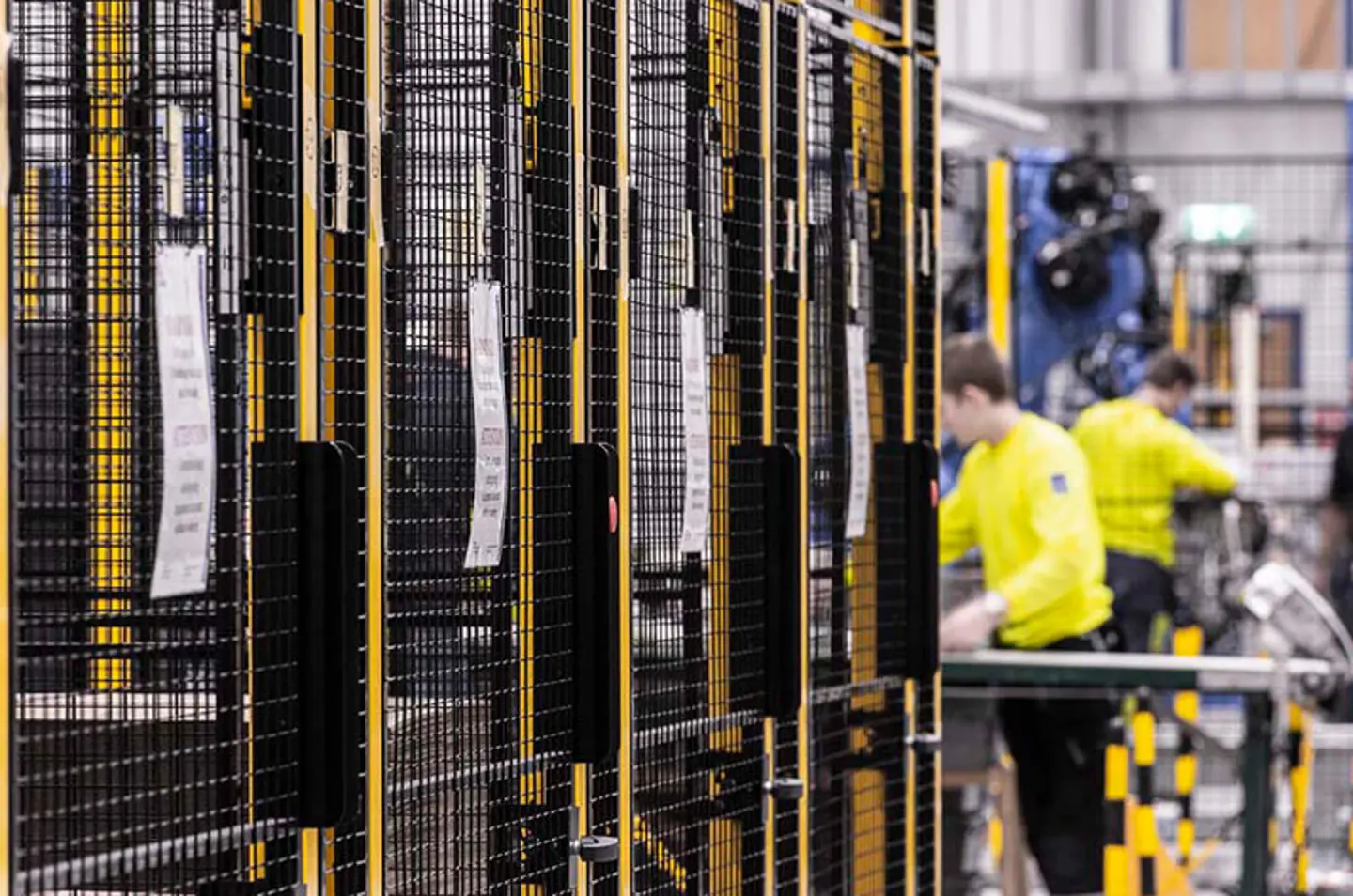 Werknemers in een fabriek, naast zwart-gele veiligheidsbarrières met metalen gaaspanelen