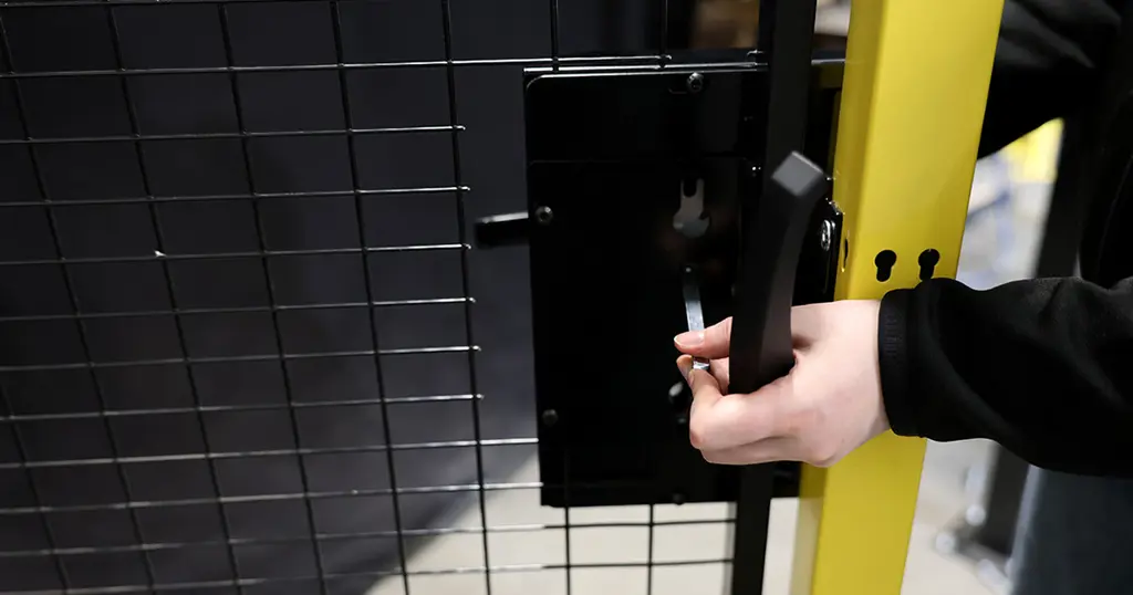 Hand die een cilinderslot vasthoudt op een zwart gaaspaneel